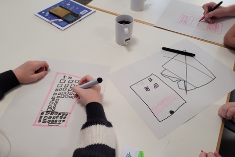 Kinder malen Handys auf ein Blatt Papier.